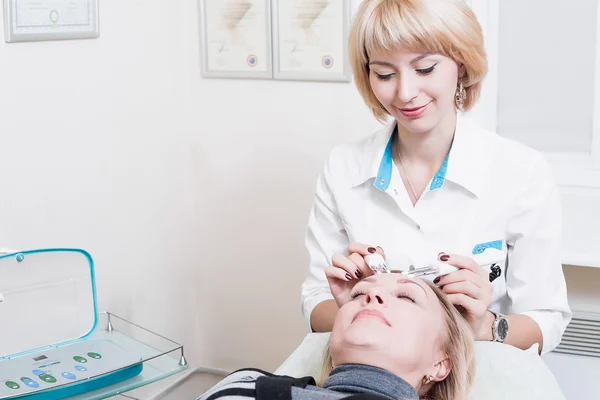 güzel genç sarışın kadın kalıcı güzellik uzmanı hasta ile ofiste beyaz bir elbise içinde. Doktor. gülümseyen