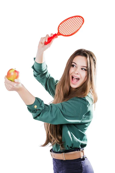 Junges schönes Mädchen in grüner Bluse, das einen Apfel hält und mit einem Tennisschläger lächelt. Apfel will den Schläger treffen. isolieren — Stockfoto