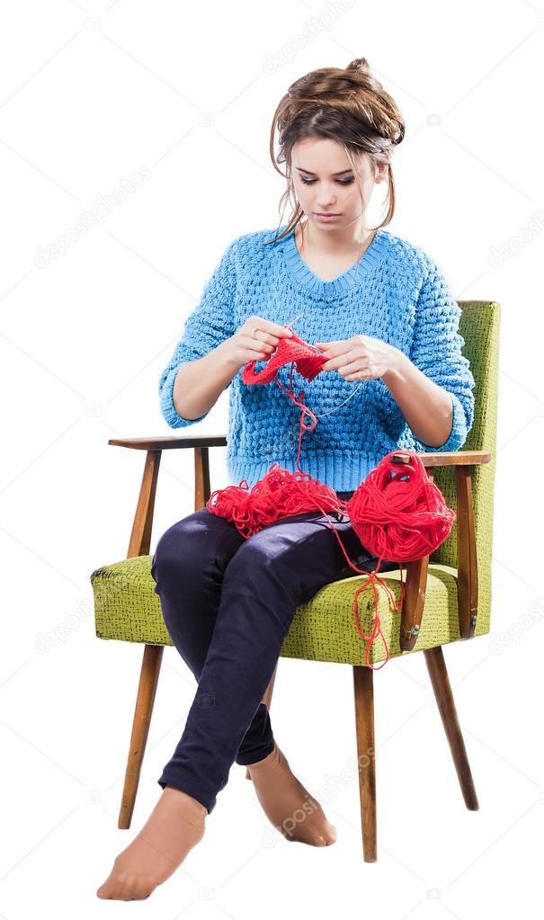 tortured young girl in a  sweater sits on a chair with a red ball of yarn and knitting a scarf and Spitz. Tired. White background. 