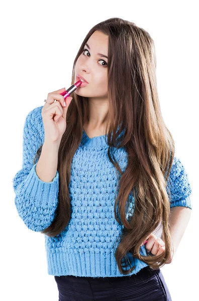 Schönes junges Mädchen in blauem Pullover, das auf weißem Hintergrund steht und einen roten Lippenstift in der Hand hält. gefärbte Lippen. — Stockfoto