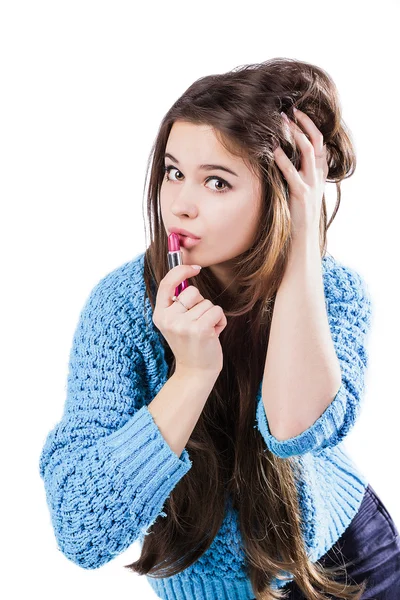 Beautiful young girl in a blue sweater standing on a white background and holding a red lipstick. Dyed lips. — Stock Photo, Image