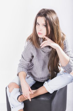 Beyaz bir arka plan üzerinde siyah bir peruk oturan örme kazak güzel kız. Uzun siyah saçlı. yırtık kot pantolon