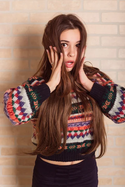 Krásná dívka v různobarevných pletený svetr stojí u cihlové zdi. Poblíž okna. — Stock fotografie