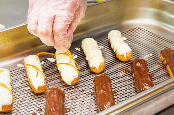 Pastry eclairs decorated with black and white chocolate and orange rind