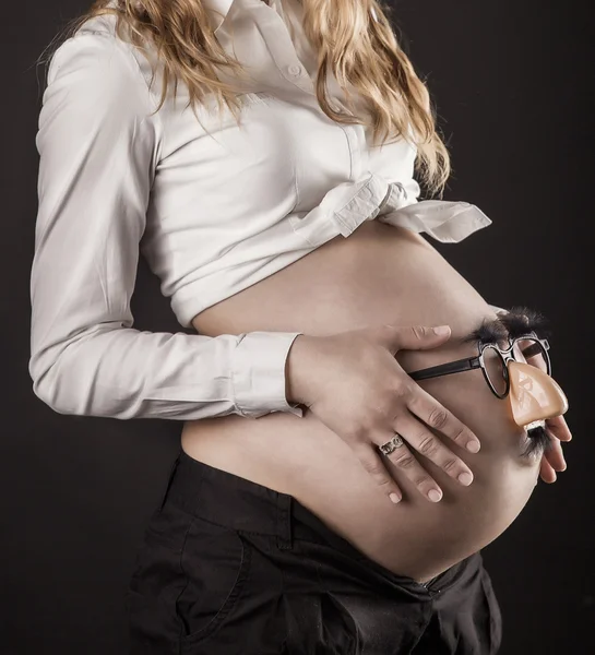 Gelukkig zwangere vrouw met grappige bril op haar buik, close-up, op zwarte achtergrond — Stockfoto