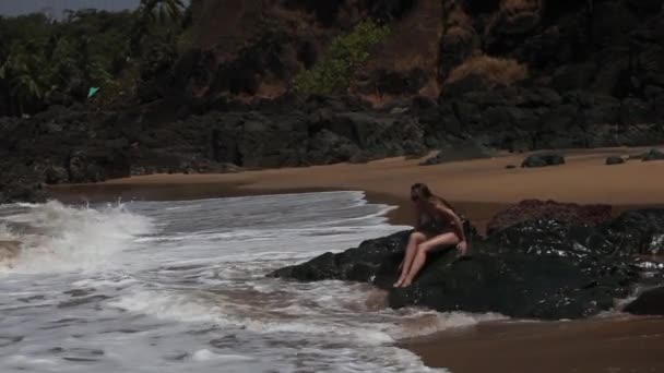 Mujer sentada en una roca en la playa con olas . — Vídeos de Stock