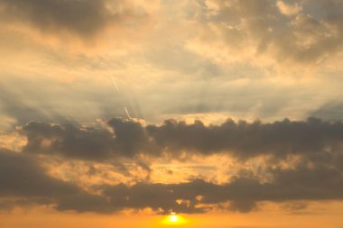 Parlak güneş ışığıyla dramatik bulut oluşumu yoğun ışınlarla bulutların arasından geçip turuncu gökyüzünü etkileyici bir şekilde aydınlatıyor..