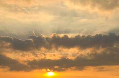 Parlak güneş ışığıyla dramatik bulut oluşumu yoğun ışınlarla bulutların arasından geçip turuncu gökyüzünü etkileyici bir şekilde aydınlatıyor..