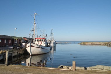 Mavi gökyüzünün altında tekneleri ve kırmızı ahşap kulübeleri olan Idyllic balıkçı limanı.