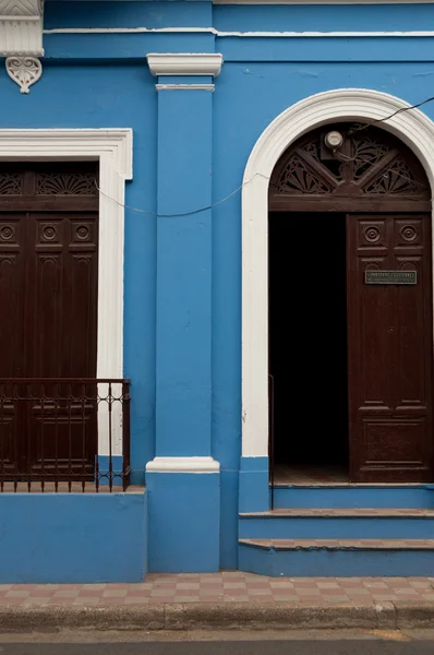 Blue stone wall of colonial house with brown wooden open door in Granada