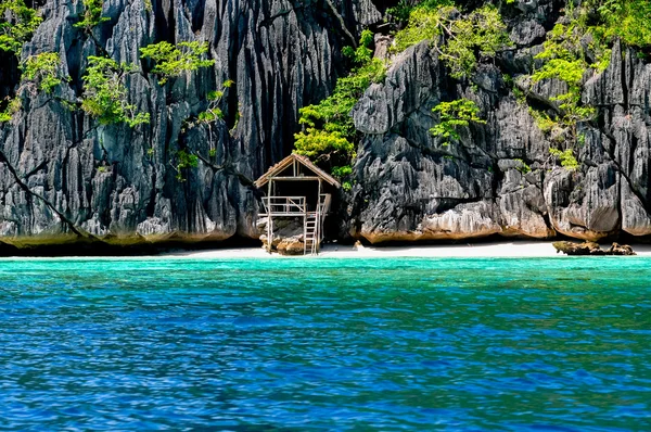 Lonely wooden bamboo house on stilts at a small hidden beach of rocky island — Stock Photo, Image