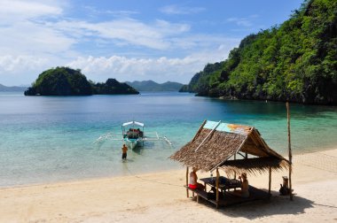 Kel adam beyaz kum Plajı'nda bir bambu köyde iki kadın dinlenme süre ahşap geleneksel filipino tekne çekerek