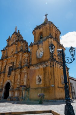 Beyaz saat ve mavi gökyüzü altında üstte bir çan ile sarı Kilisesi önünde eski latern