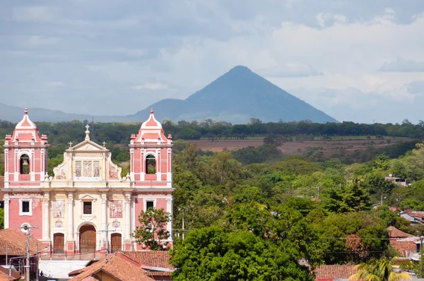 Große rosa Kirche, die vor einem Bergvulkan und Bäumen steht, leon — Stockfoto