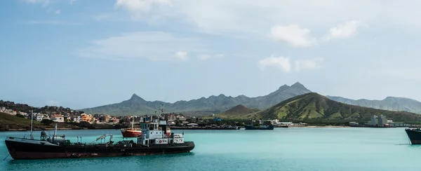 Fartyget framför småstad på blå havet kusten med molnigt berg bakgrund, Kap Verde ön — Stockfoto