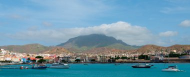 Mavi okyanus kıyısındaki küçük bir kasabanın önünde bulutlu dağ arkaplanlı tekneler Senegal açıklarındaki Cape Verde Adası 'nda.