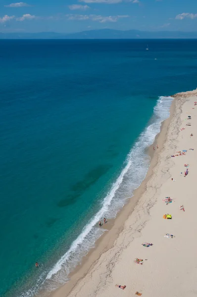 Playa amarilla de arena limpia con gente tomando el sol junto al mar mediterráneo en la costa de Tropea — Foto de Stock