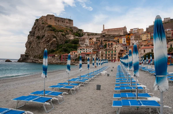Sombrilla azul y silla de playa en la playa frente a la pequeña ciudad italiana en el acantilado bajo el cielo azul — Foto de Stock