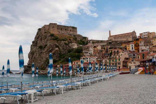 Blå paraply och beachchair på stranden framför lilla italienska staden på klippa under blå himmel — Stockfoto