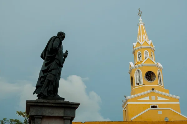 Estátua preta e torre de relógio amarelo na frente de um céu azul — Fotografia de Stock