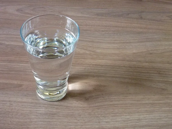 Un vaso de agua sobre una mesa de madera — Foto de Stock