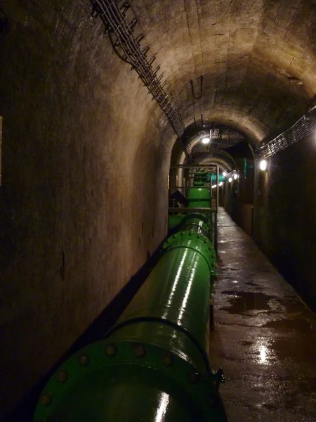 Underjordisk tunnel med en grön vattenledning — Stockfoto