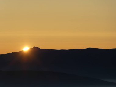 Tepenin ardındaki vadide altüst olmuş bulutların üzerinde gün doğumu.