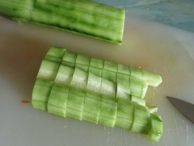 Mutfaktaki beyaz tahtada çiğ salatalık kesiyor.