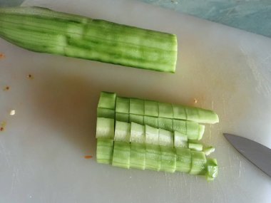 Mutfaktaki beyaz tahtada çiğ salatalık kesiyor.