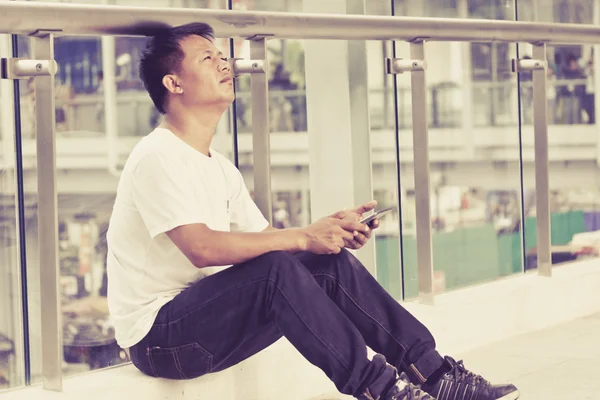 Un hombre sentado en una acera Navegar por Internet y en el teléfono inteligente —  Fotos de Stock