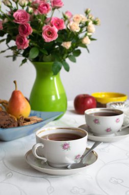 Çay saati. Siyah çay beyaz masa örtüsü üzerinde iki bardak şeker, meyve, çerez ve gül vazo kase ile. Seçici odak. Antika arka plan.