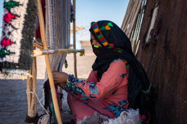 Erg Chebbi, Morocco - April 12, 2016: A berber woman weaves using a traditional loom in a village near the Erg Chebbi, in Morocco. clipart