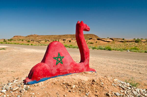 A red statue of a camel with the flag of morocco. Highway to Sahara Desert
