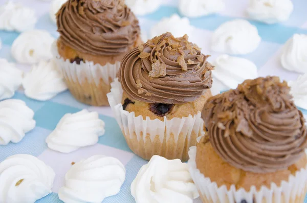 Muffins savoureux à la crème au chocolat décorés de bonbons au sucre dans une nappe à carreaux bleus et meringue — Photo