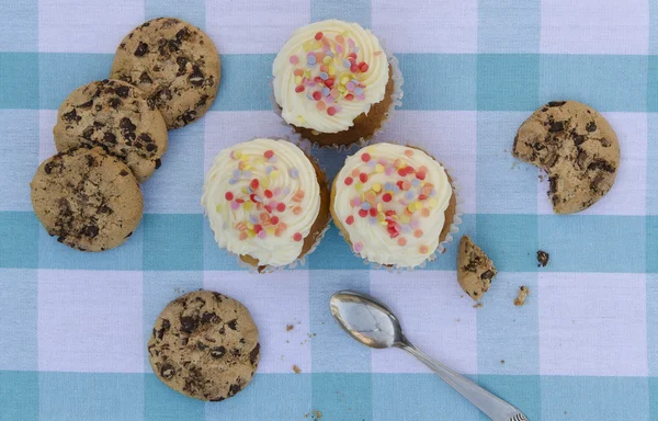 Tasty cookies and muffins cakes with vanilla cream decorated with sugar candies on a wooden background