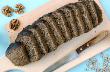 Tahta bir tahtada çavdar ekmeği. Masada ayçiçeği tohumu, fındık ve eski bıçak ile dilimlenmiş ekmek