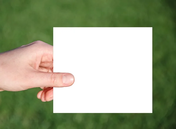 Papel de mão segurando em um fundo de grama verde — Fotografia de Stock