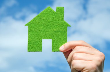 Eko ev simgesini kavramı mavi gökyüzüne bulutların arka plan üzerinde tutan el