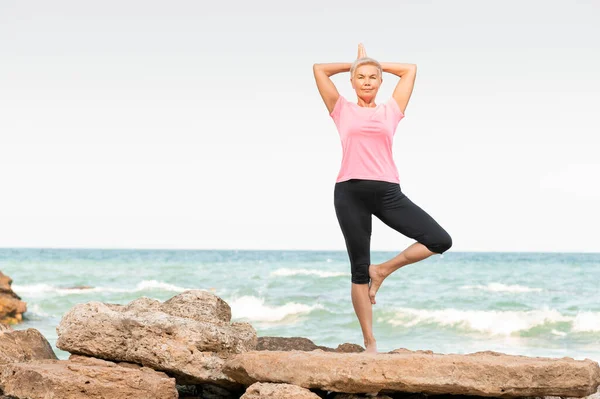 A woman standing on a rocky beach in yoga position — Stock Photo, Image