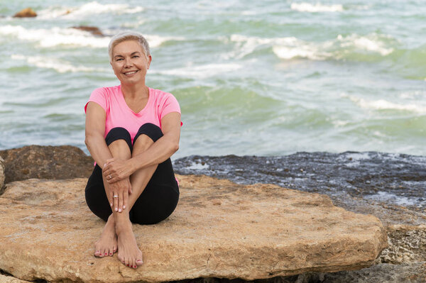 Sports mature woman sitting at the beach and smiling