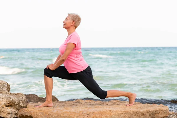 Side view portrait of mid age woman stretching on the beach — Stock Photo, Image