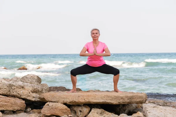 Portrait of mature woman doing yoga by sea — Stock Photo, Image