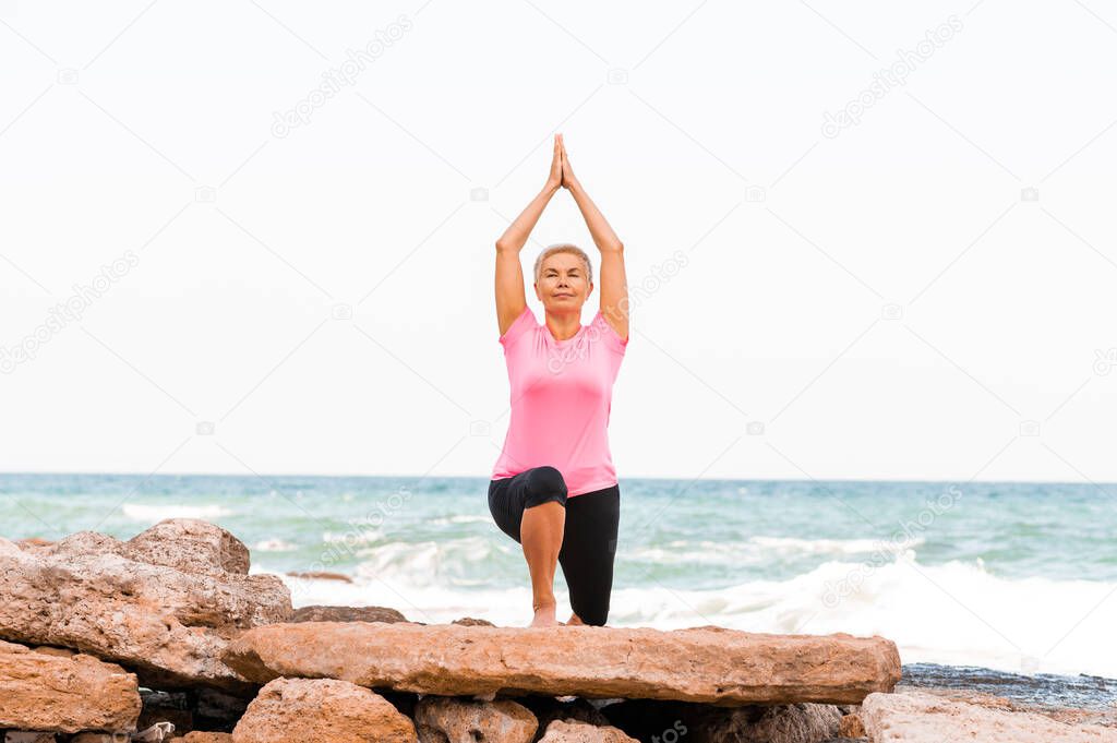 Sporty woman practicing yoga on the beach doing stretching and exercising balance.