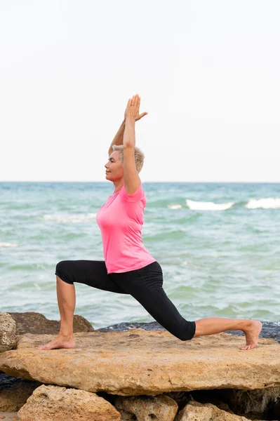 Mature woman doing pilates by the sea. Vertical side view portrait — Stock Photo, Image