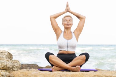 Sahilde yoga yapan yaşlı bir kadın. Model için alanı kopyala