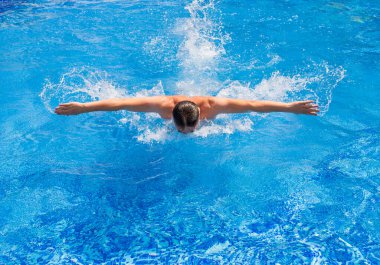 Yüzücü kelebek stilinde havuzda yüzüyor.