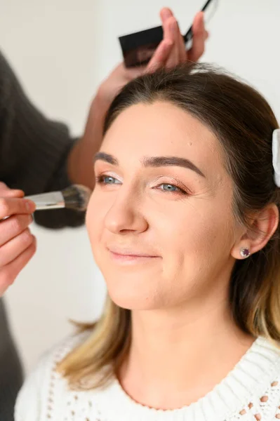 Makeup artist making professional makeup of smiling young woman. Makeup lessons