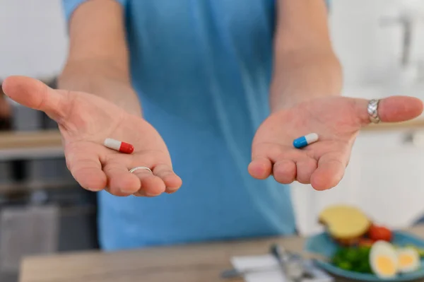 Виберіть в охороні здоров'я. Чоловік дає дві різні таблетки. Блакитна і червона таблетки, які таблетки краще — стокове фото
