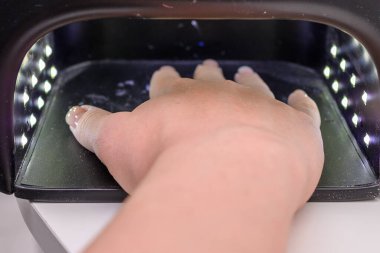 Kadın eliyle oje sürmek için öndeki ultraviyole lambayı kapat. Güzellik salonu konsepti