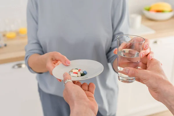 Close up Senior weibliche Hände halten ein Glas Wasser und nehmen eine Reihe von Vitaminen und Pillen — Stockfoto
